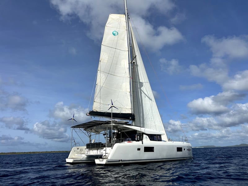2018 Lagoon 42 catamaran sailing with full sails deployed, showcasing its sleek white hull and spacious cockpit under a bright blue sky.