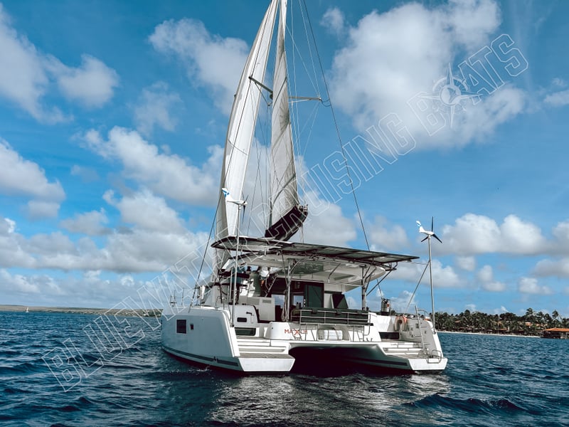 Sleek exterior of a 2021 Lagoon 42 catamaran sailing in open waters, featuring a spacious deck and fully raised sails against a vibrant sky.